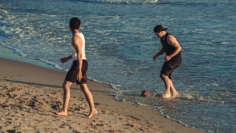 a couple of men standing on top of a sandy beach